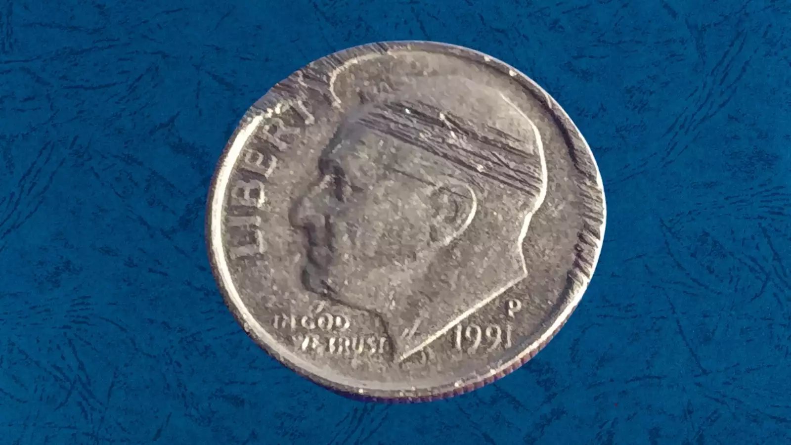 1991 Roosevelt dime with a raised die crack error line across the obverse surface, visible as a raised metal ridge